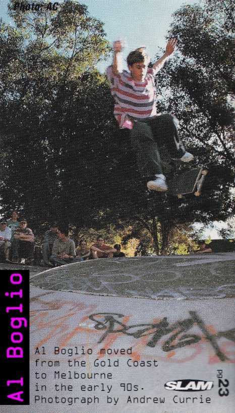Photo of Al Boglio performing a hardflip mid-air over a concrete hip at Prahran Bowl.
    Al is wearing a pink and purple striped t-shirt. His arms are raised high in the air, as he is about to land. 
    A group of spectators wearing 90s style skate fashion watch in the background.