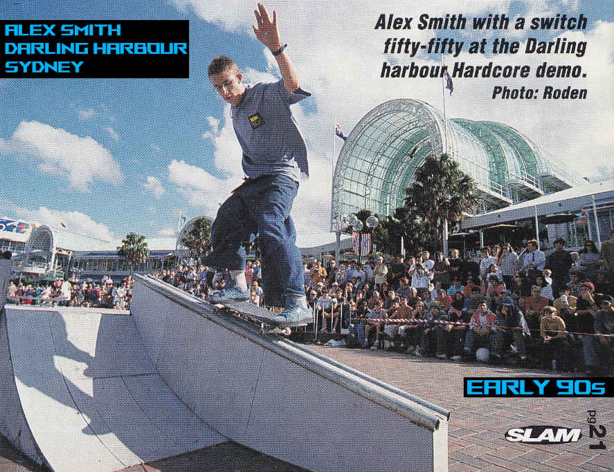 Alex gliding on top a handrail made for skate demonstrations from a platform with ramps. 
    The photo was taken on a bright sunny day with clouds in the sky.
    There is a big crowd of spectators watching in the background behind a fence.