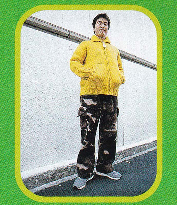 90s photograph of a man wearing a bright yellow knitted jacket with camo-style pants.