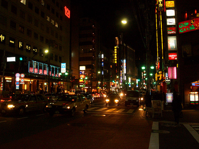 Taxis and cars move through the night amongst colored lights
  in Minato Ward - Tokyo.