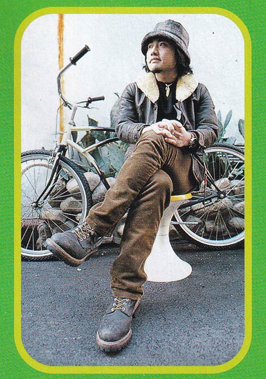 Photo of a man sitting in front of bicycle wearing vintage American style clothes.