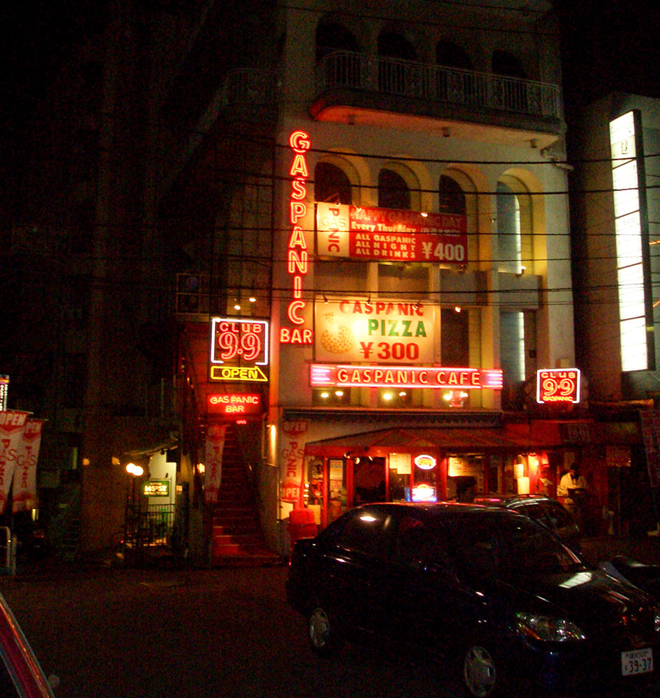 Bright, glowing signs adorn the entrance to the Gaspanic building in Roppongi. 
        Photograph by Sean Kavanagh.