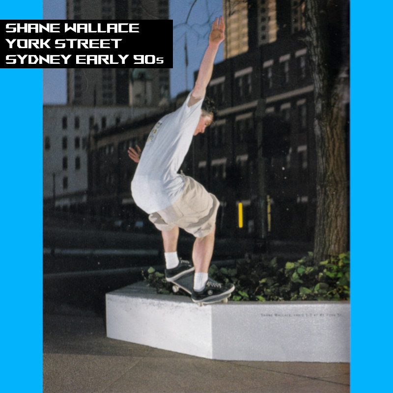 Photograph of Shane Wallace skating in the early evening. Shane is wearing baggy shorts, a t-shirt and suede Airwalk shoes.
    There are no people on the streets apart from Shane and the atmosphere is silent.